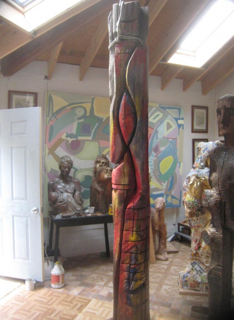Tall dark painted sculpture standing among works in a studio