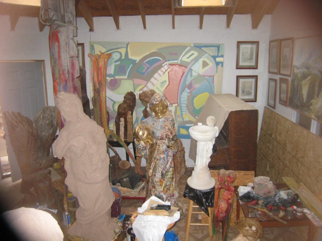 Crowded studio interior with carved figures and colorful paintings