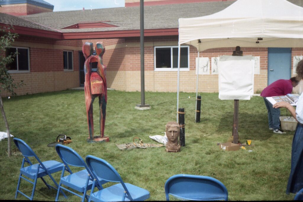 Outdoor sculpture display with a tall figure and rows of chairs