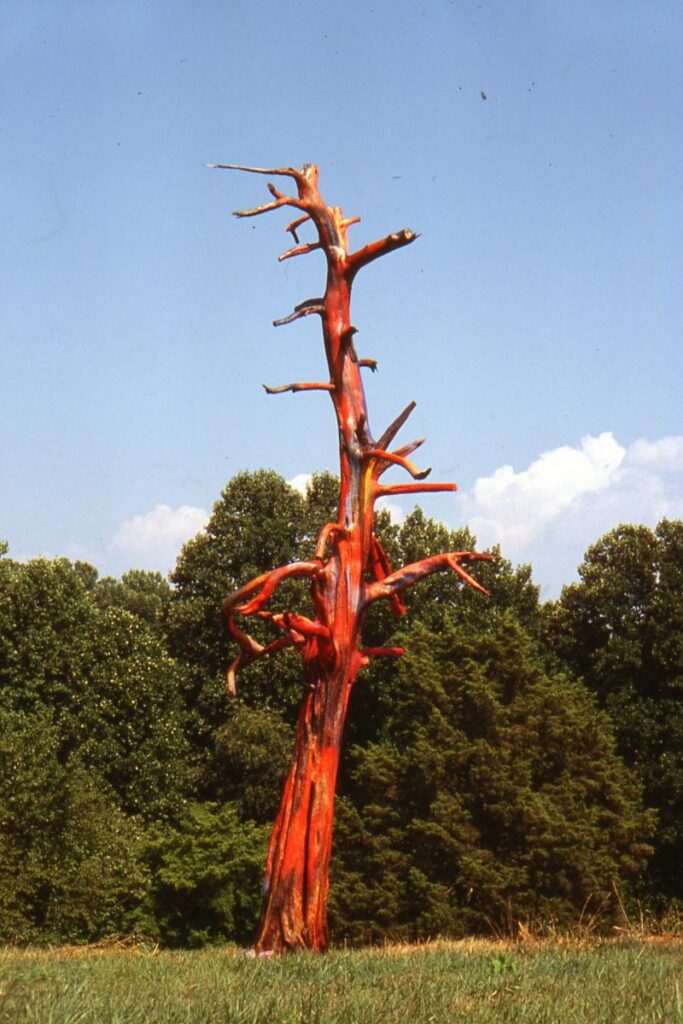 Bright red tree-like sculpture installed in a meadow