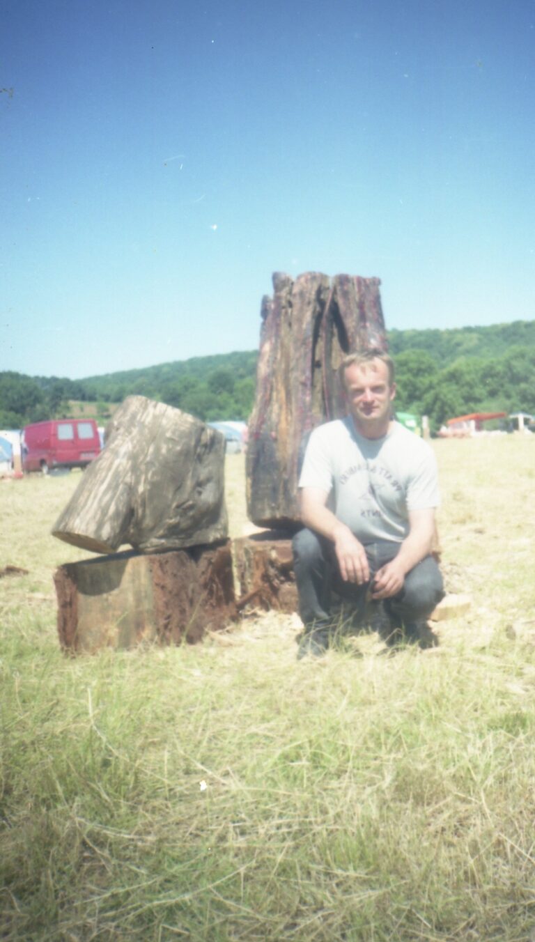 Archival photograph of Mirosław Rydzak seated beside outdoor sculpture