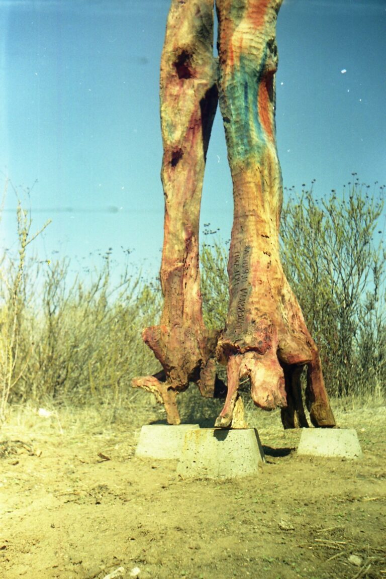 Tall outdoor sculpture ending in two carved leg-like forms