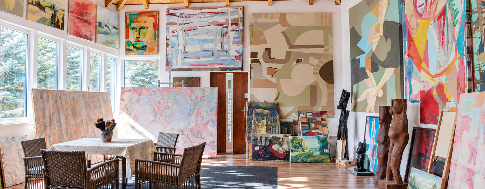 Artist studio filled with paintings and sculptures beneath a timber ceiling