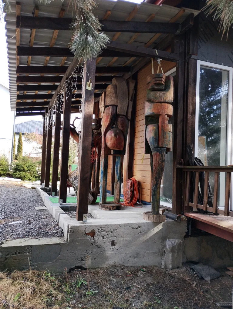 Carved wooden sculptures arranged beneath a covered studio porch