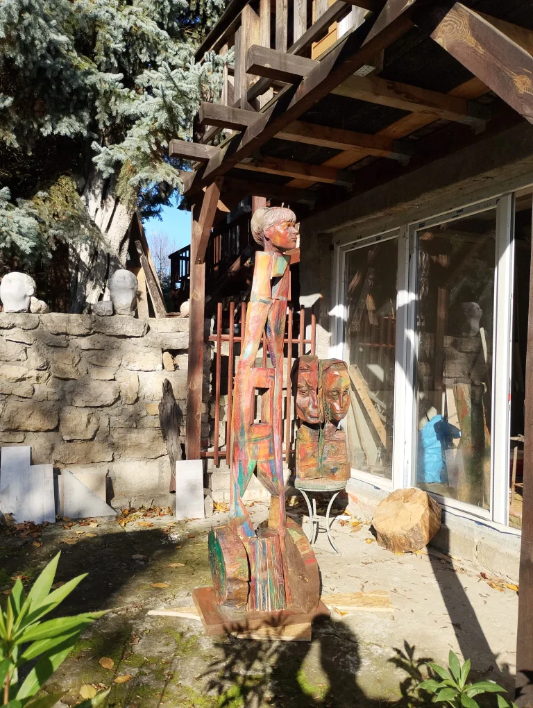Tall red and orange carved wooden figure beside a stone wall